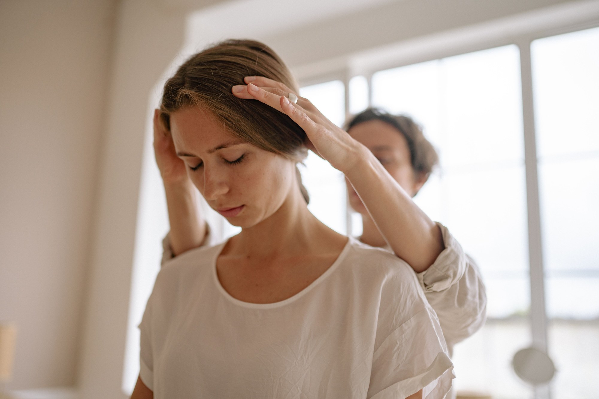 Osteopat holder hendene rundt hodet og nakken til en pasient som står med lukkede øyne